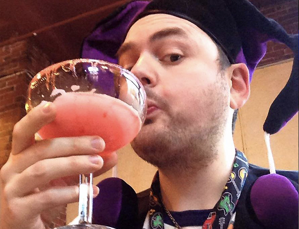 Gerry sipping a raspberry margarita wearing a jester hat