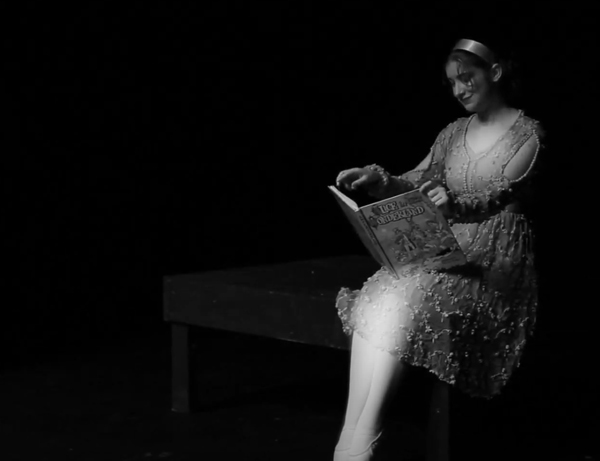 Maren as Alice sitting on a platform reading Alice's Adventures in Wonderland